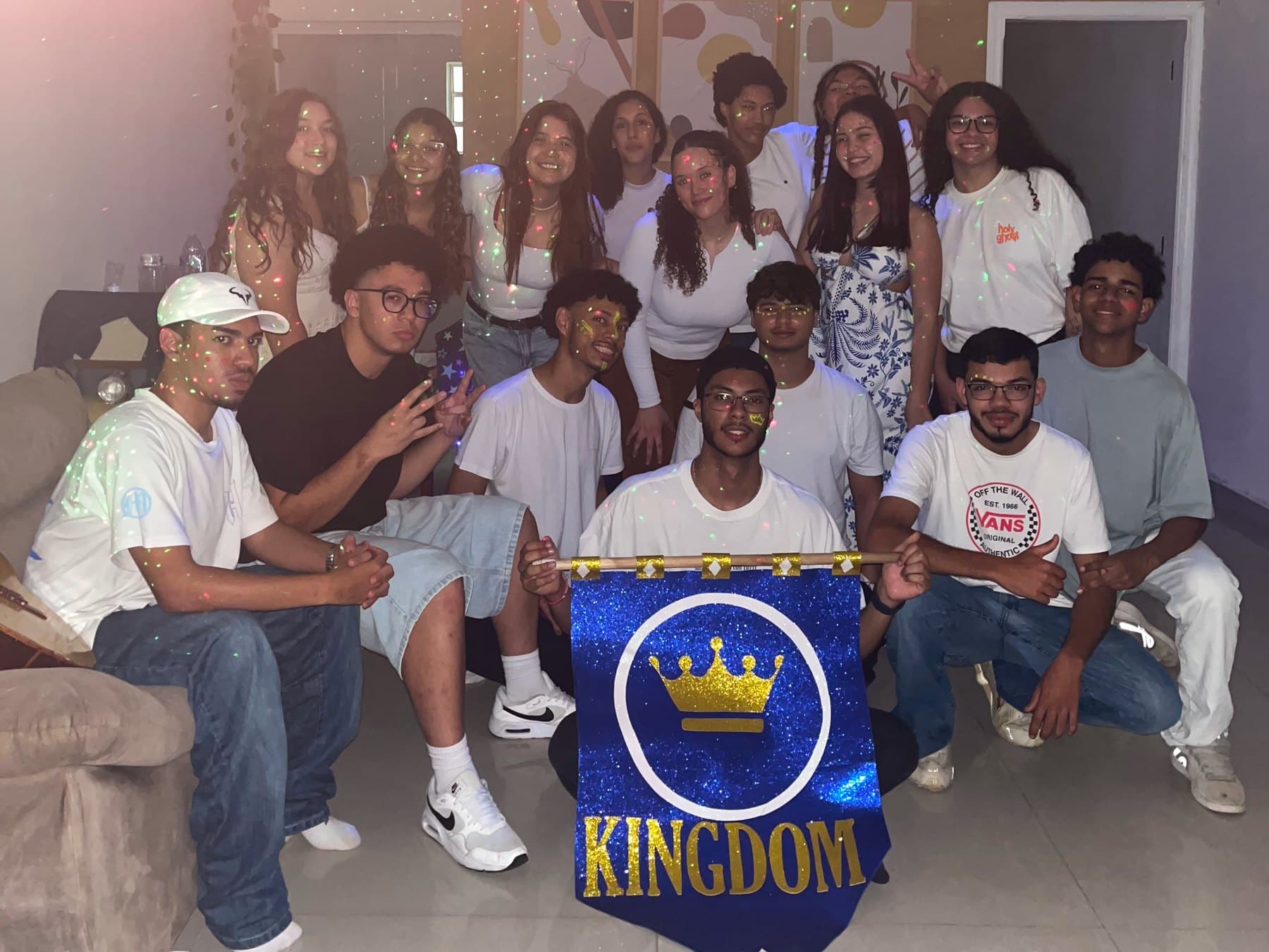 Turma de jovens da célula Kingdom reunida numa sala, segurando um estandarte azul com uma coroa dourada