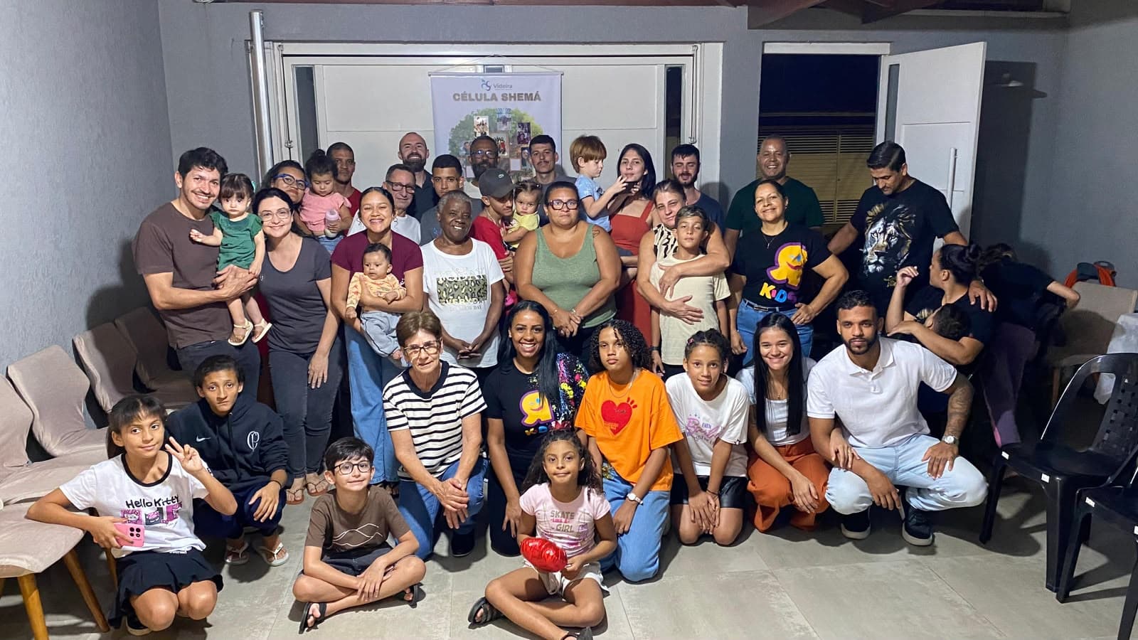 Roda de pessoas amontoadas na sala de estar de uma casa, rindo, sob a luz quente do abajur