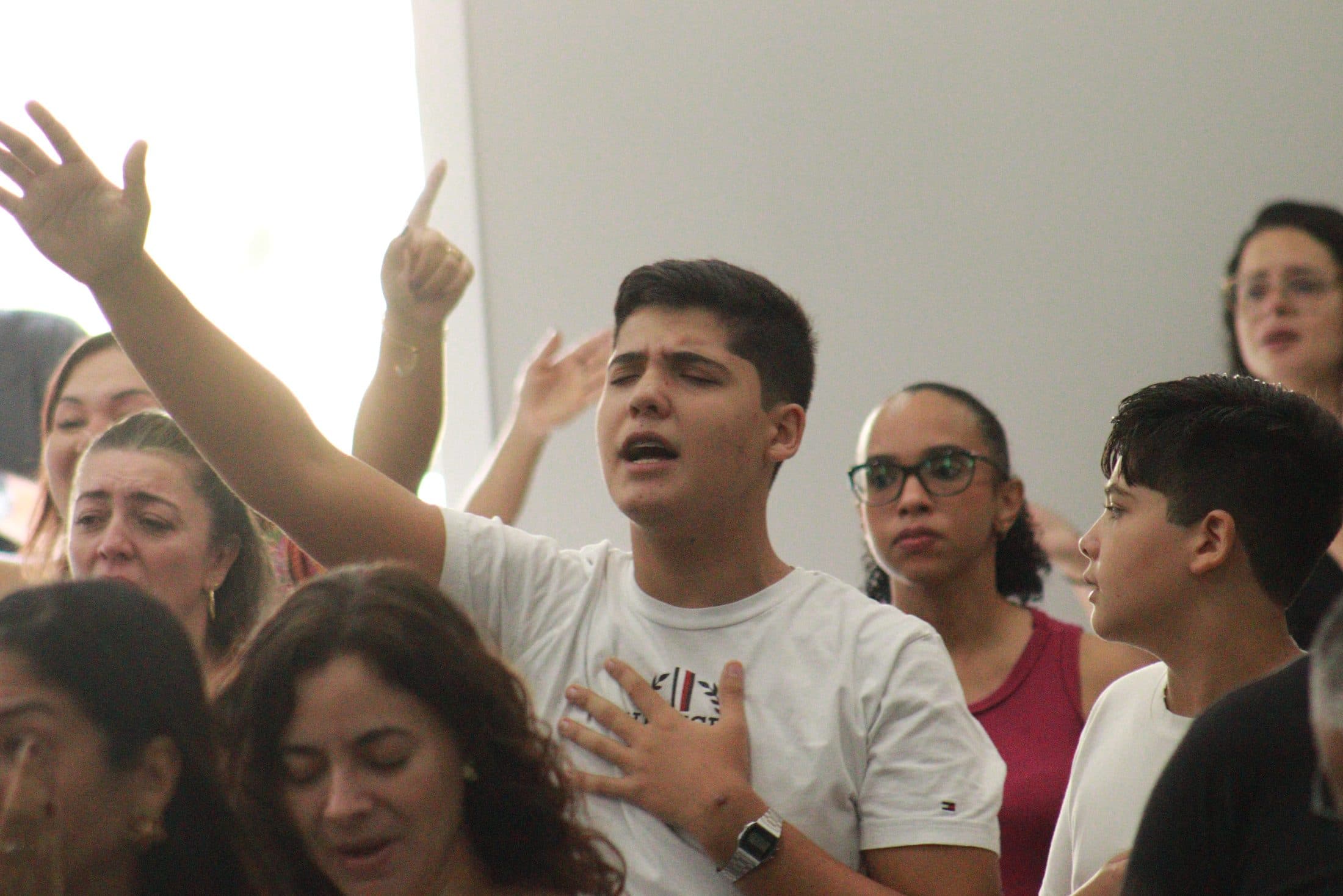 Jovem da Videira em adoração num culto, uma das mãos erguida e a outra sobre o peito