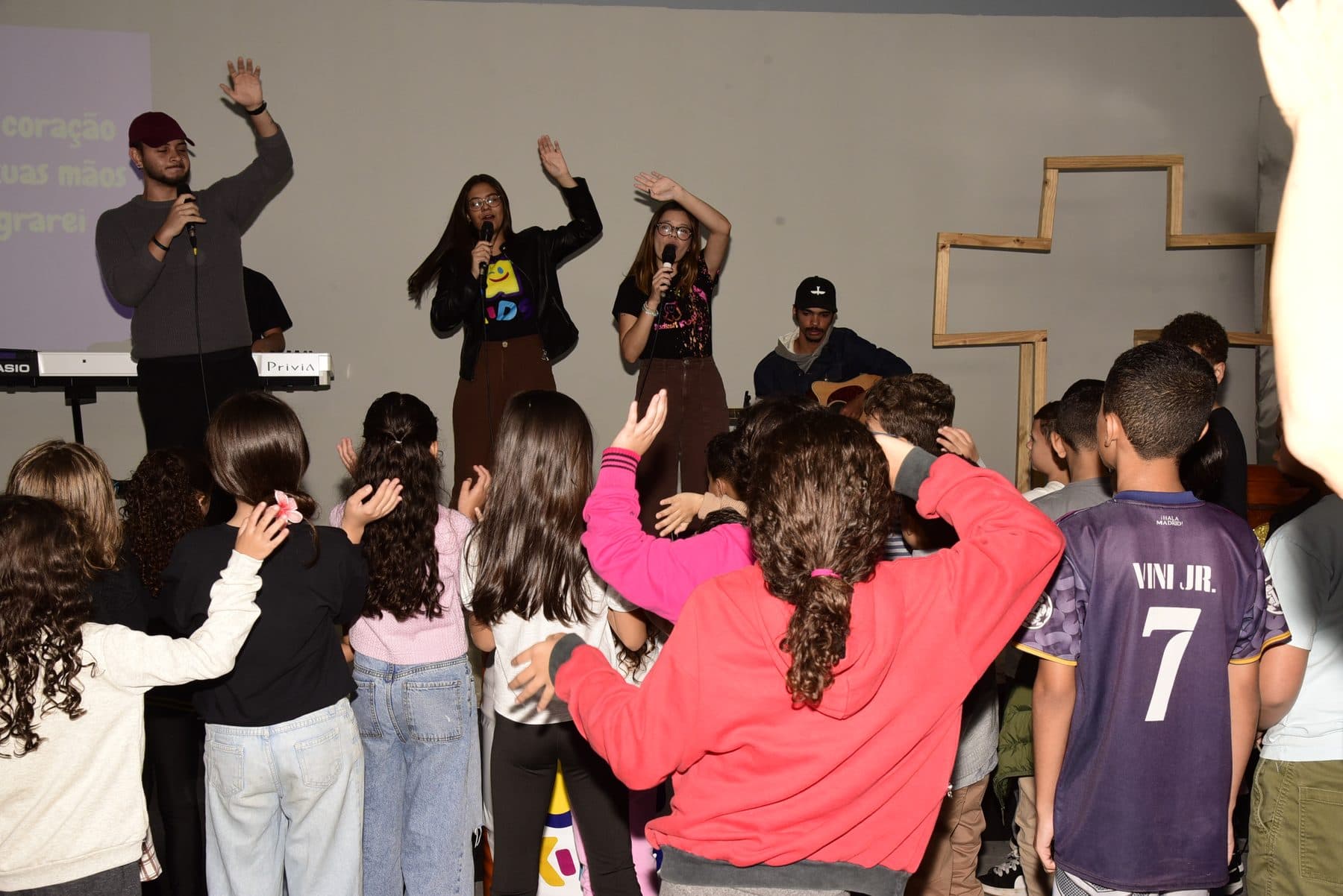 Crianças de mãos levantadas no louvor, com a equipe ministrando à frente