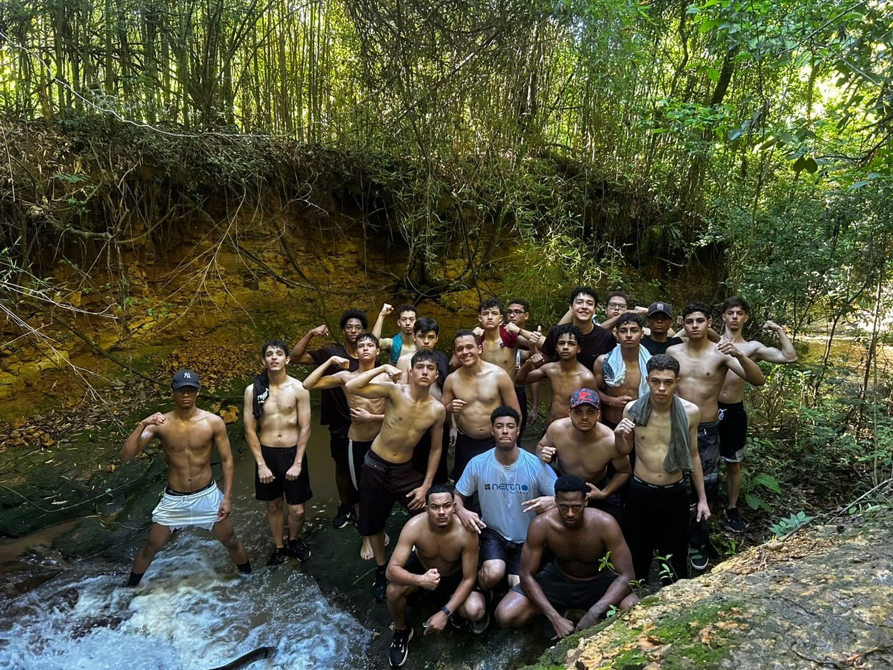 Grupo de rapazes dentro de um riacho no meio do mato, posando para a câmera