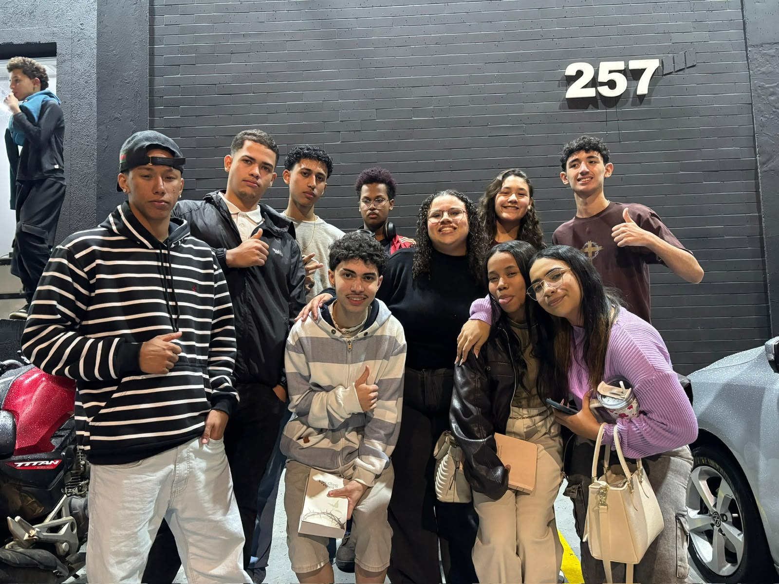 Grupo de jovens posando na calçada à noite, embaixo do número 257 no portão