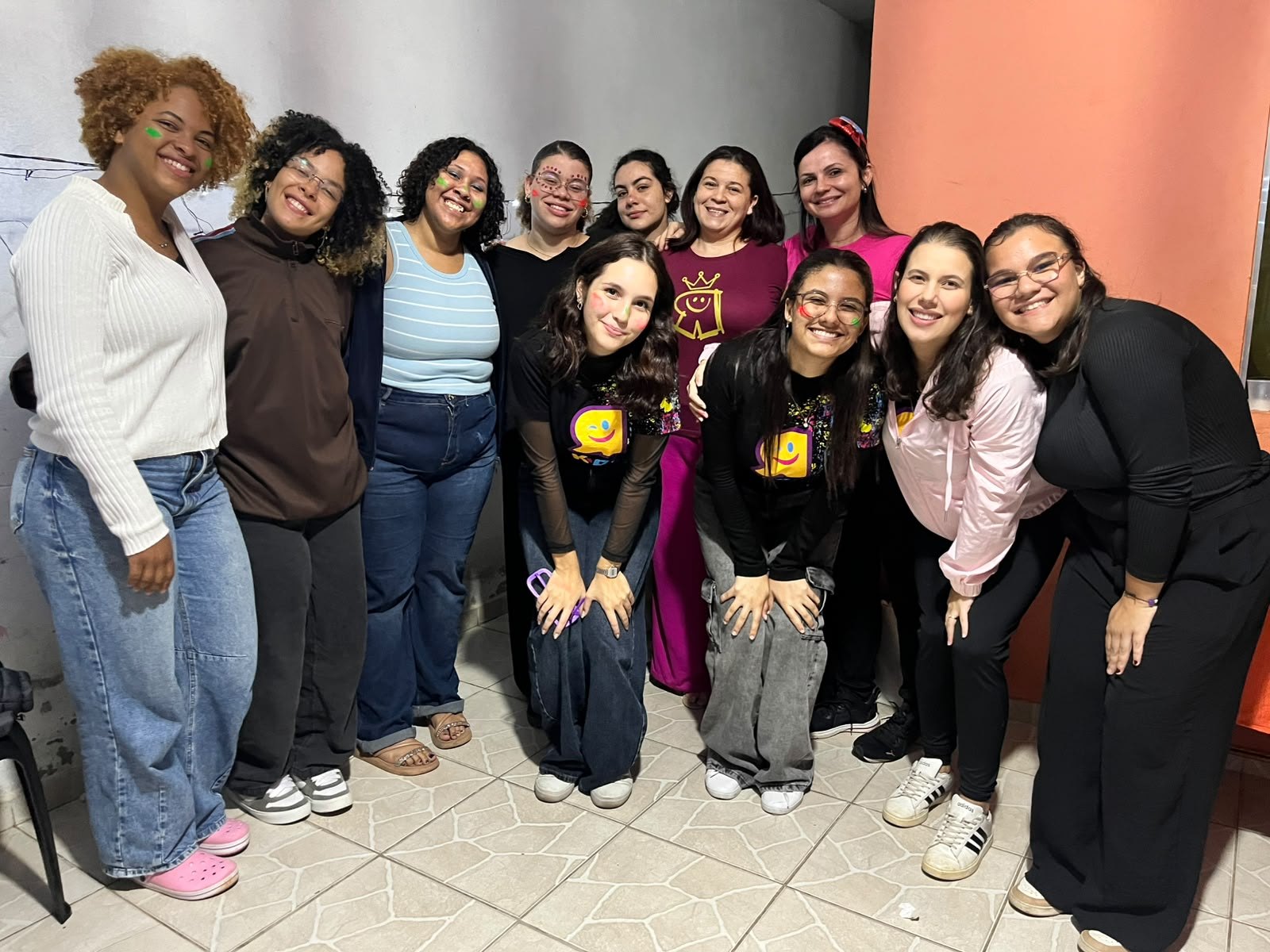 Grupo de moças posando lado a lado diante de uma parede laranja