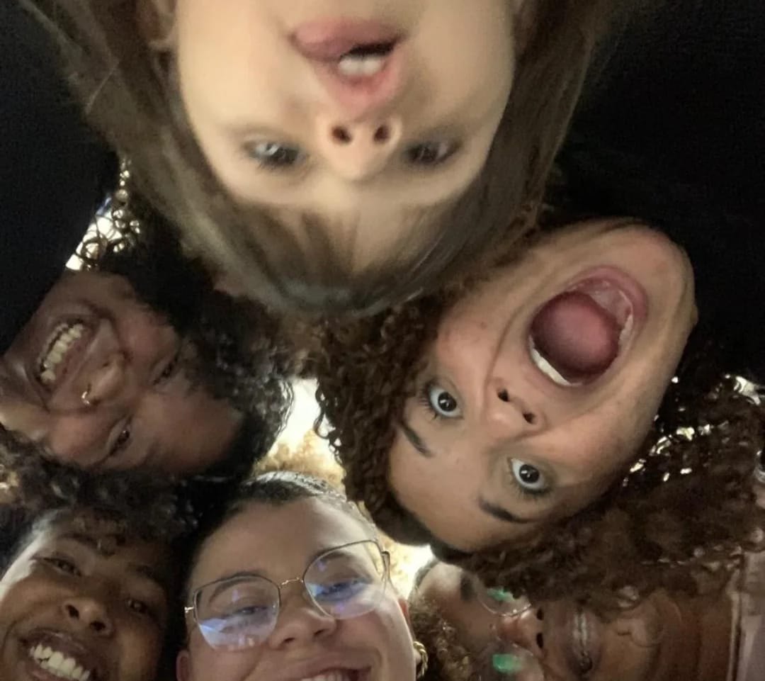 Selfie tirada de baixo, com cinco rostos de jovens amontoados sobre a câmera, todos rindo e fazendo careta